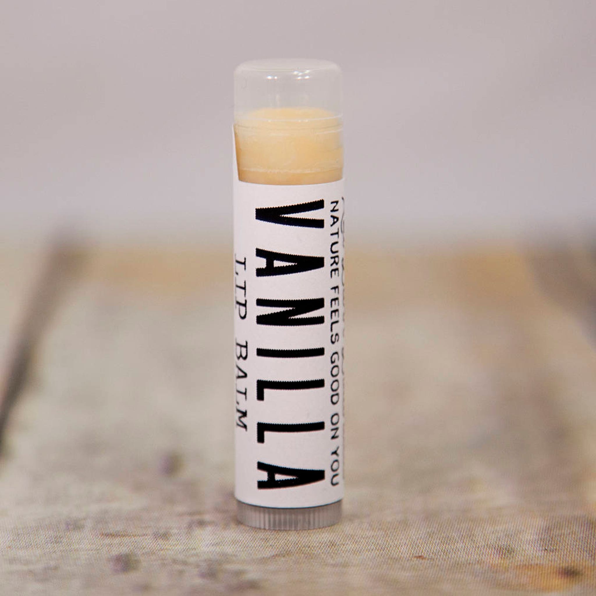 Lip balm tube with white label, vanilla text, and clear cap, on wooden surface