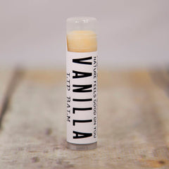 Lip balm tube with white label, vanilla text, and clear cap, on wooden surface