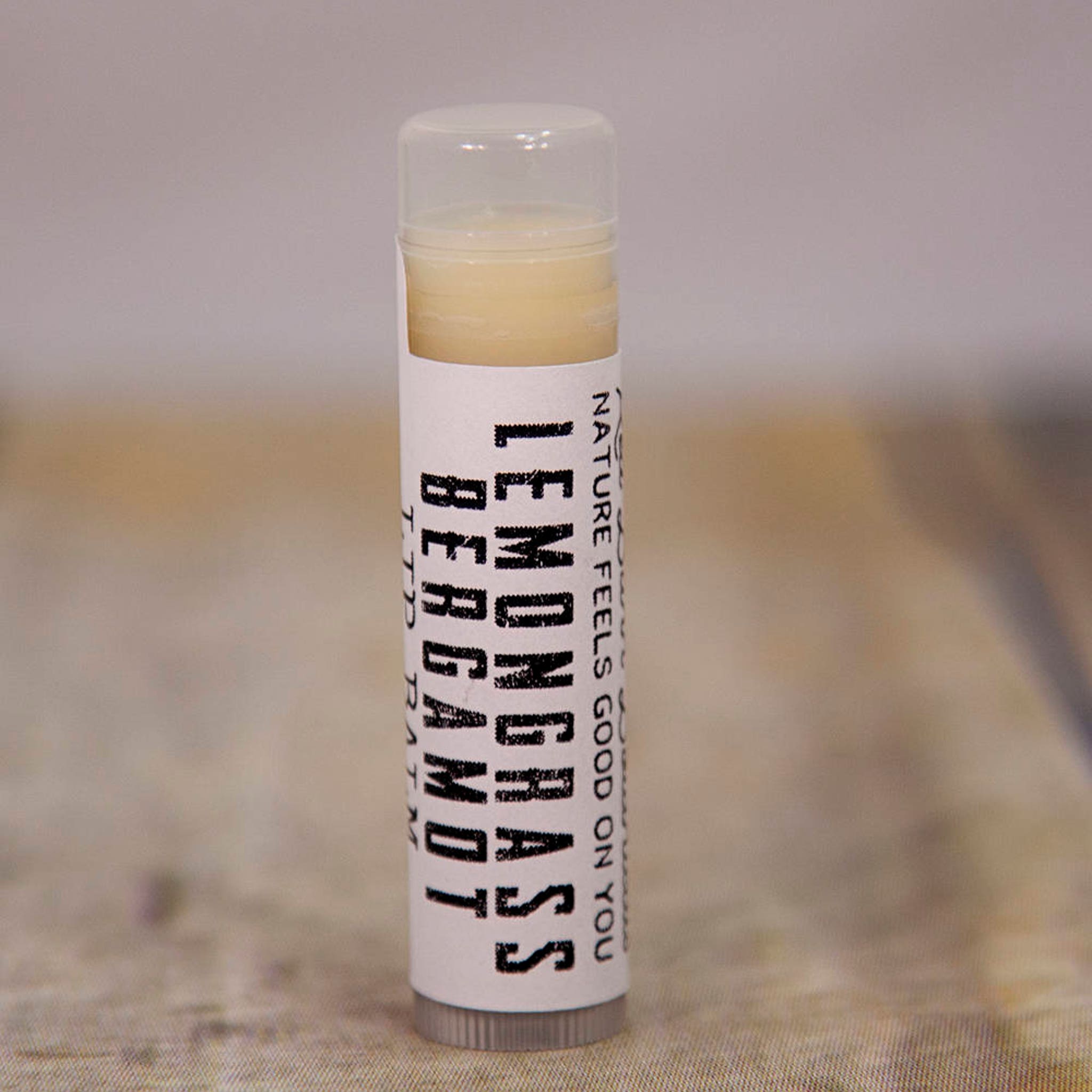 Lip balm tube with clear cap, white label, and yellow balm inside, "Lemongrass Bergamot" text