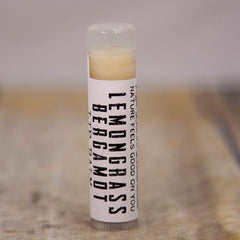 Lip balm tube with clear cap, white label, and yellow balm inside, "Lemongrass Bergamot" text