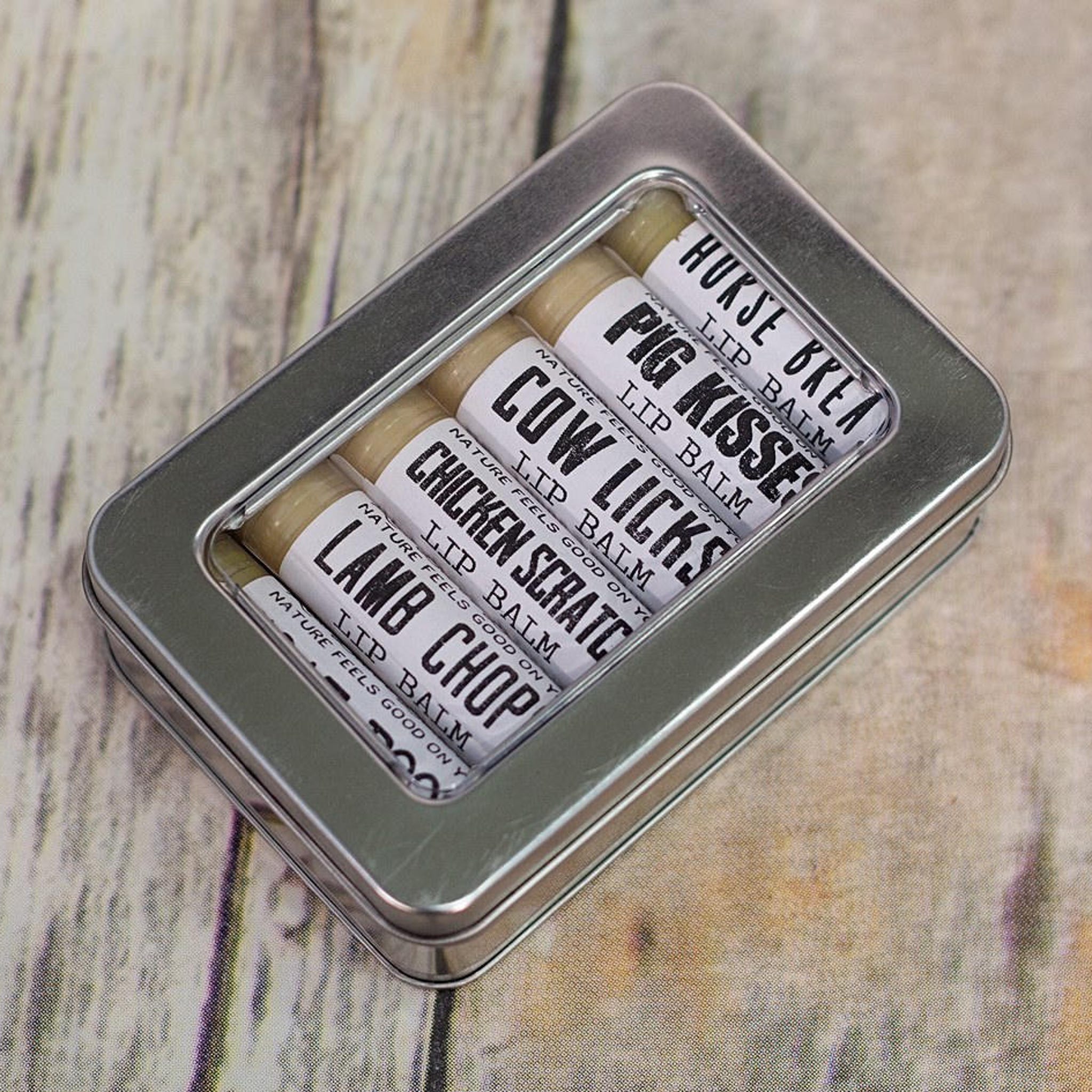 Lip balm set in a silver metal tin with white labels and black text, on a wood background