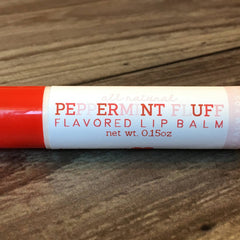 Lip balm tube with red and white label, "Peppermint Fluff" text, on wood surface