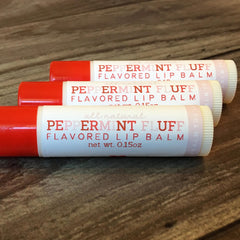 Lip balm tubes with red caps, white and pink text, and ribbed texture on wood surface
