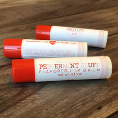 Lip balm tubes with red and white packaging, visible text, and wooden surface background