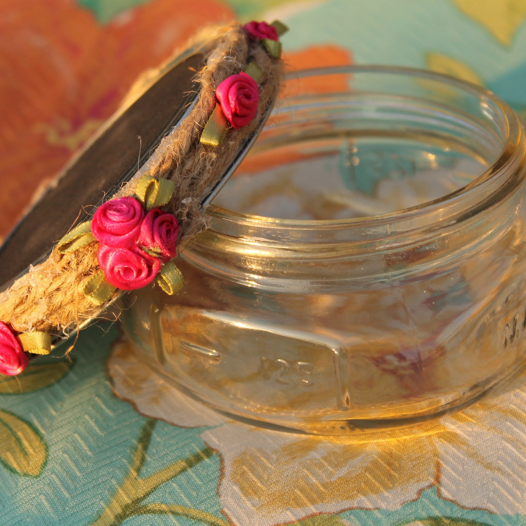 Glass jar with pink rose accents, jute twine, and clear glass body on patterned fabric