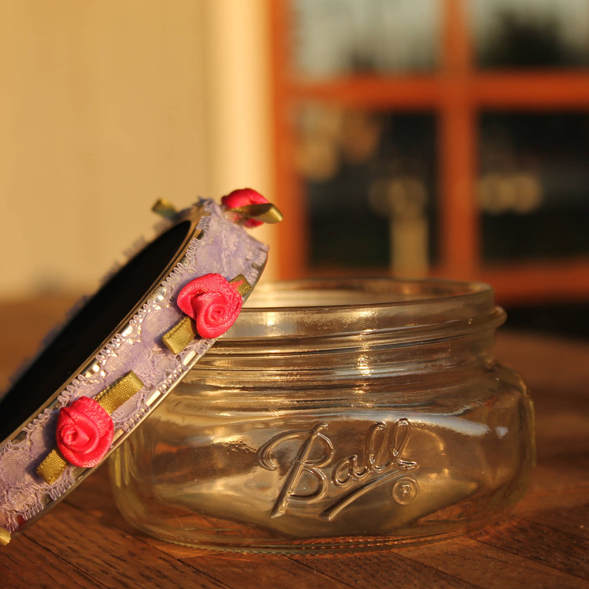 Glass jar with Ball logo, floral accent, and pink rose detail on a wooden surface