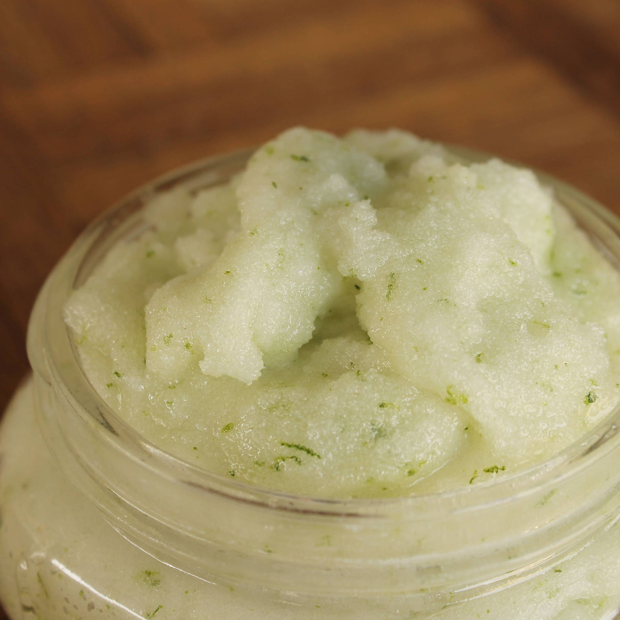 Body scrub in a glass jar, light green color with dark green flecks, close-up shot