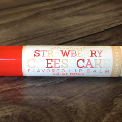 Lip balm tube with red and white label, Strawberry Cheesecake text, on wood grain background