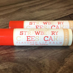 Lip balm tubes with red and white labels, Strawberry Cheesecake flavor, on wood surface
