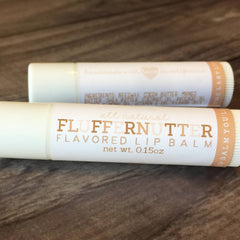 Flavored lip balm tubes, white with brown text, "Fluffernutter" label, on wood surface.