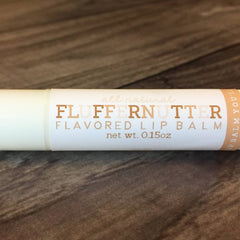 Lip balm tube with white and tan label, Fluffernutter text, and brown wooden background