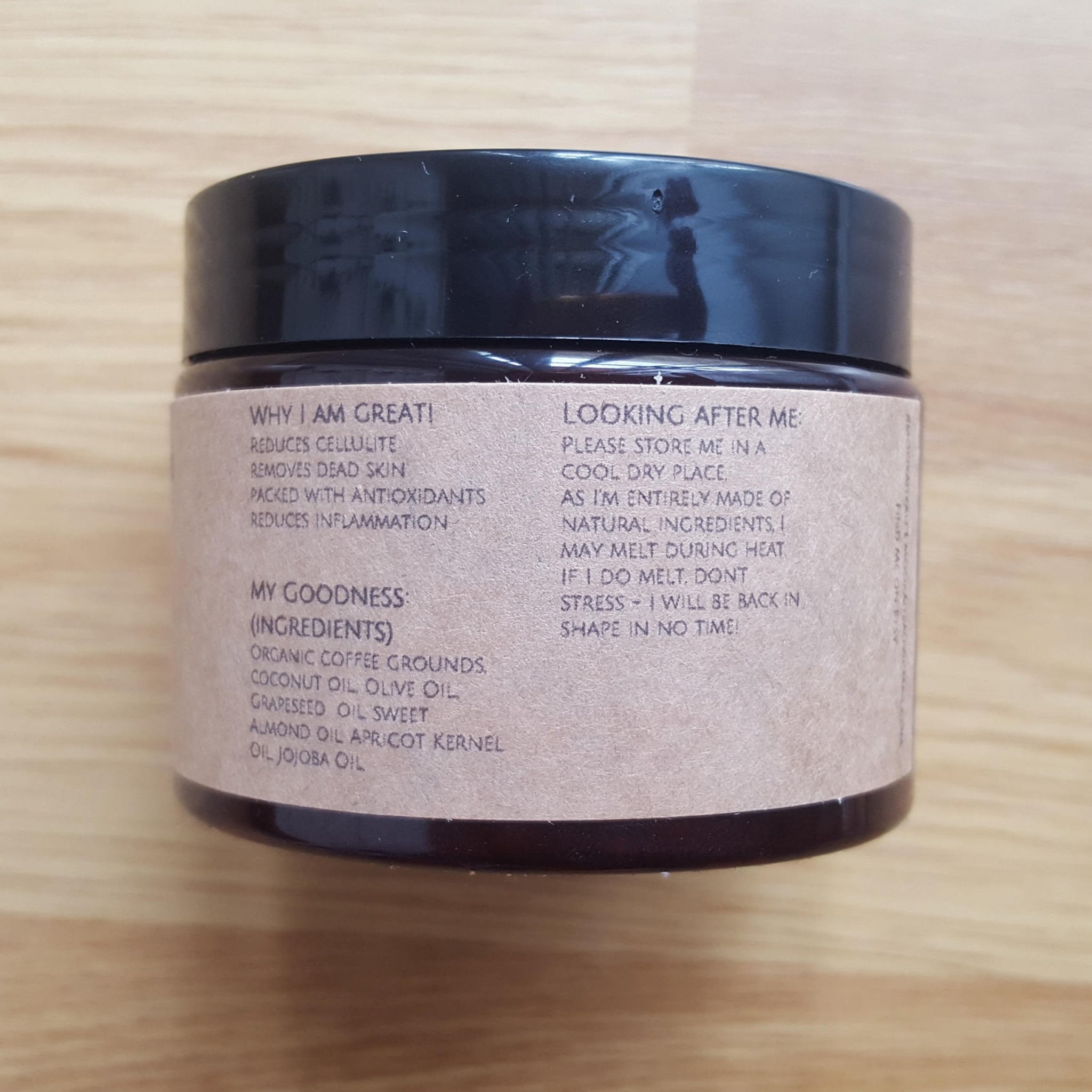 Jar of cream with black lid, tan label, and visible ingredients on wooden surface.