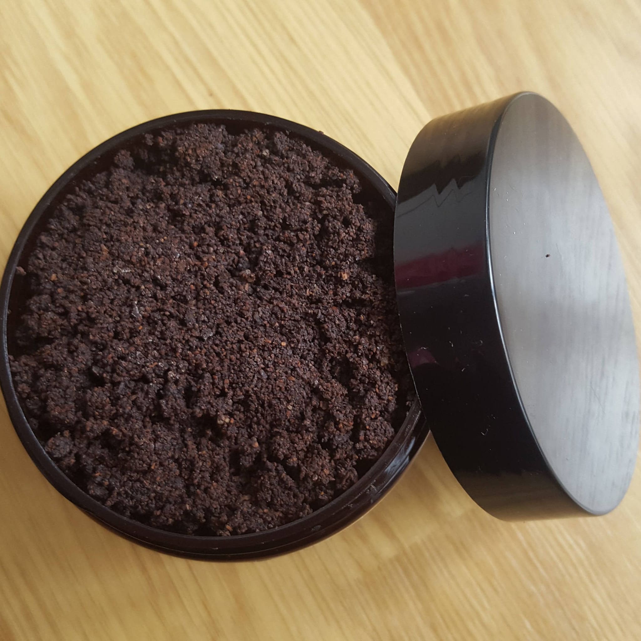 Brown granular material in black container with black lid on wooden surface