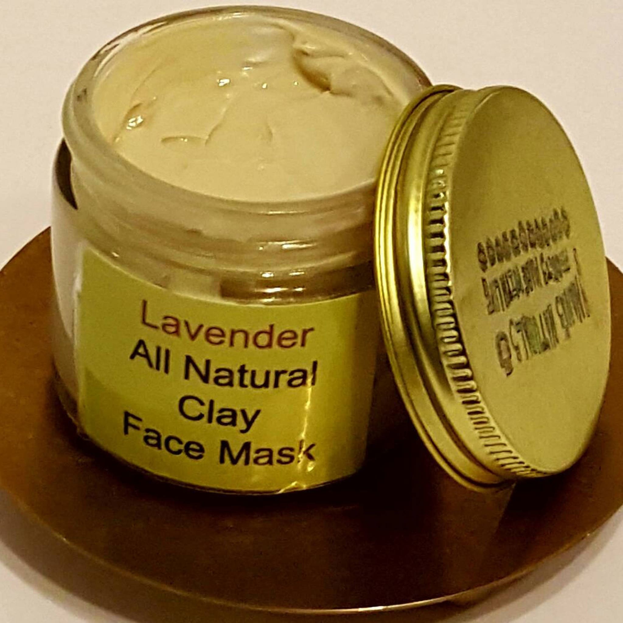 Clay face mask in a clear glass jar with a gold lid, light beige cream, and a yellow label with text