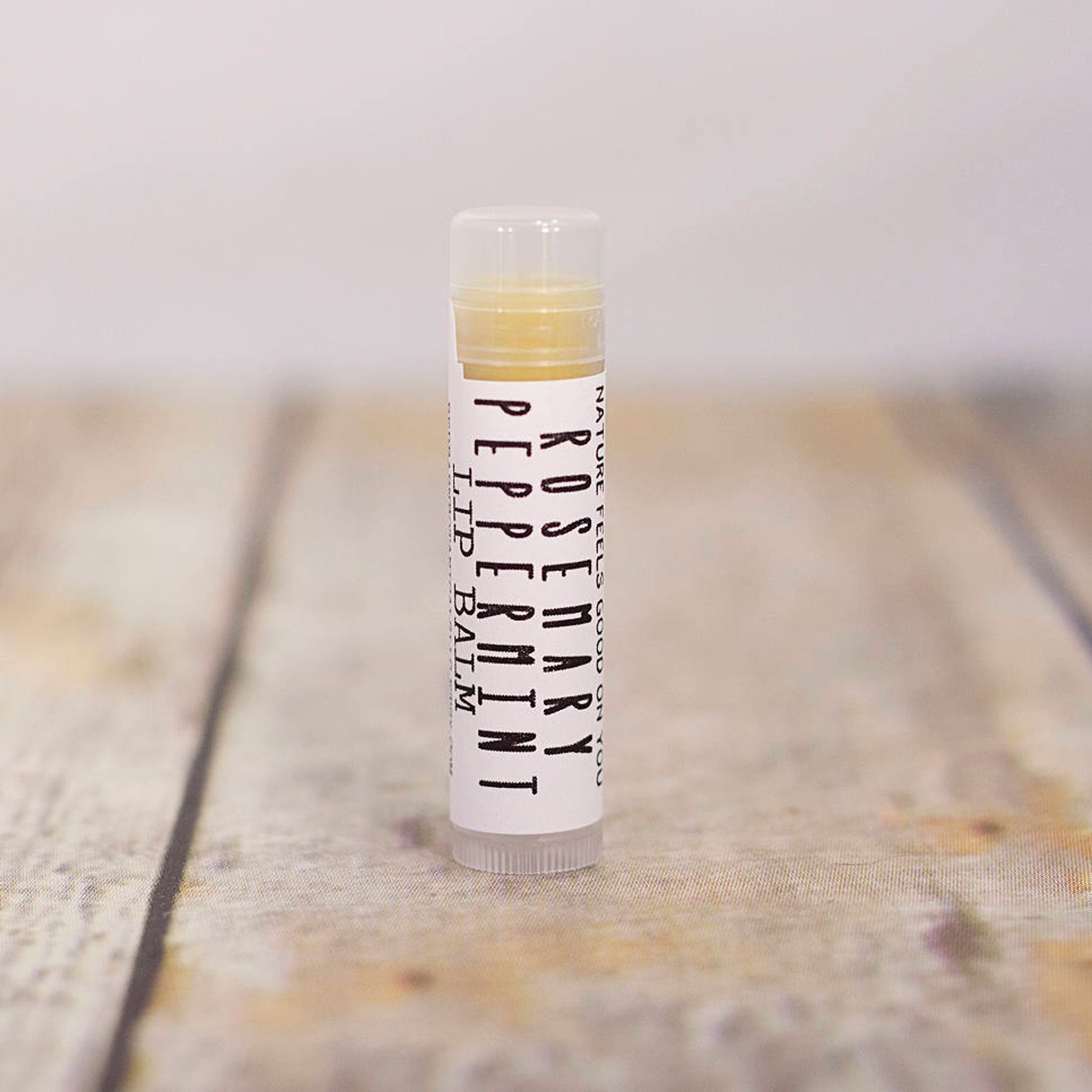 Lip balm tube with white label, clear cap, and yellow balm inside, Rosemary Peppermint text