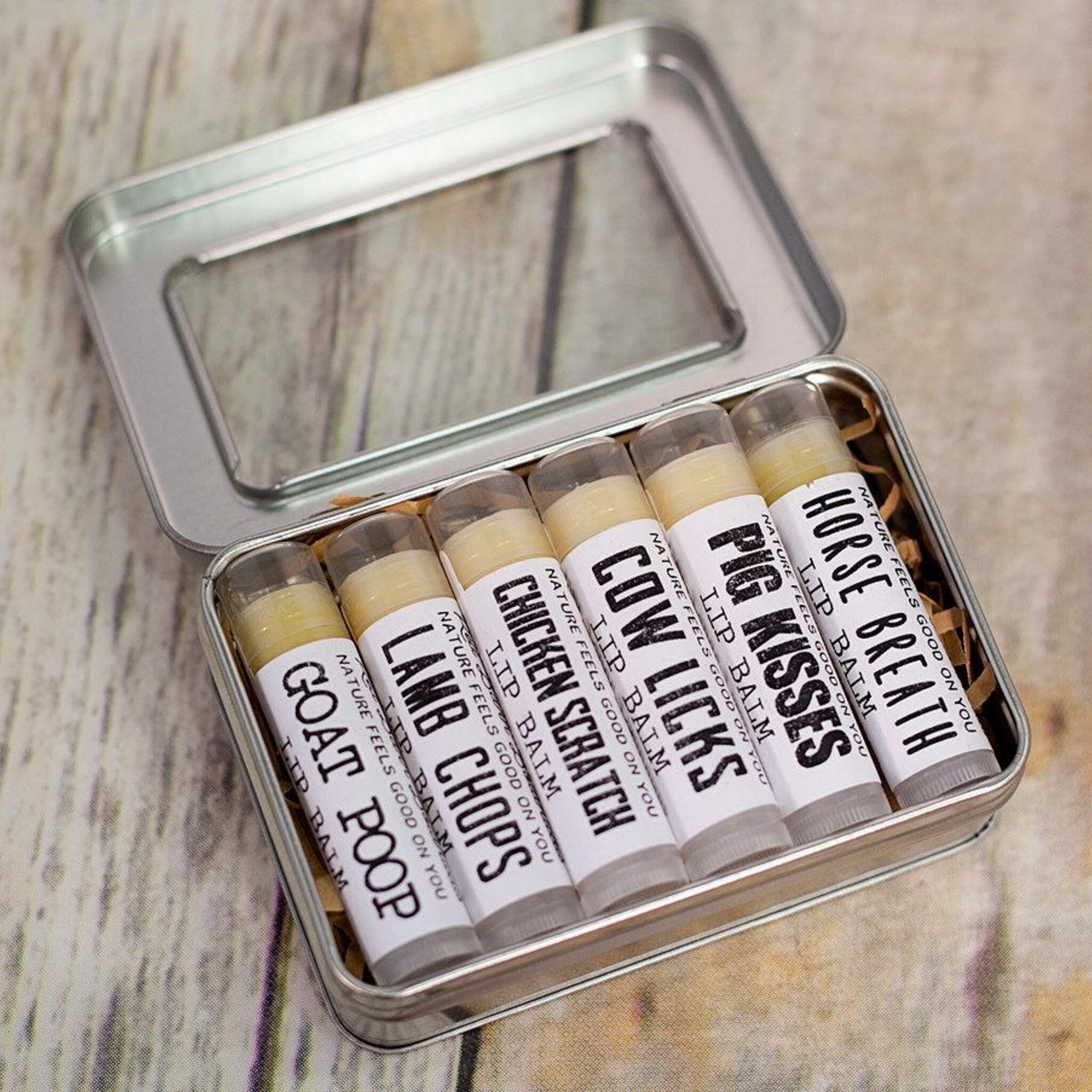 Lip balms in a metal tin, with white labels, clear tubes, and tan balm inside.