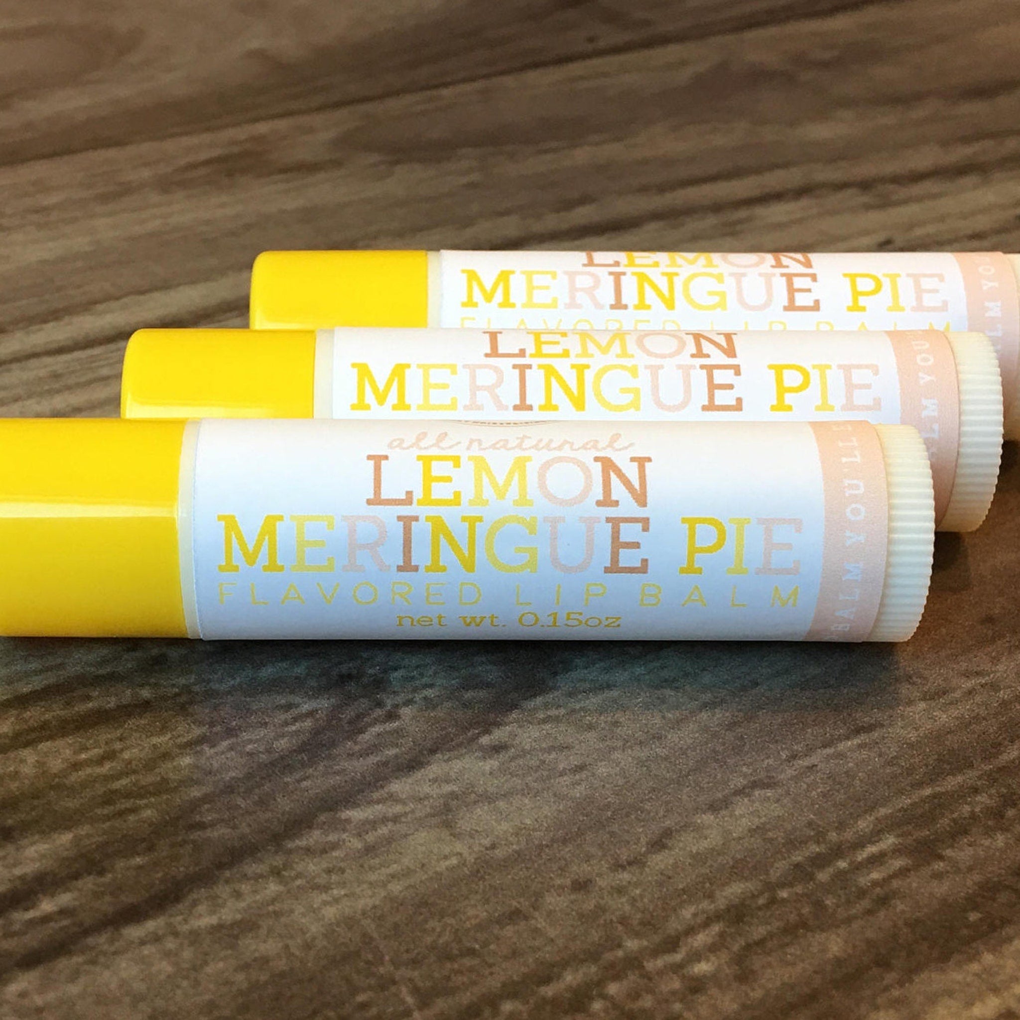 Lip balm tubes with yellow, white, and tan labels, printed "Lemon Meringue Pie" on wooden surface