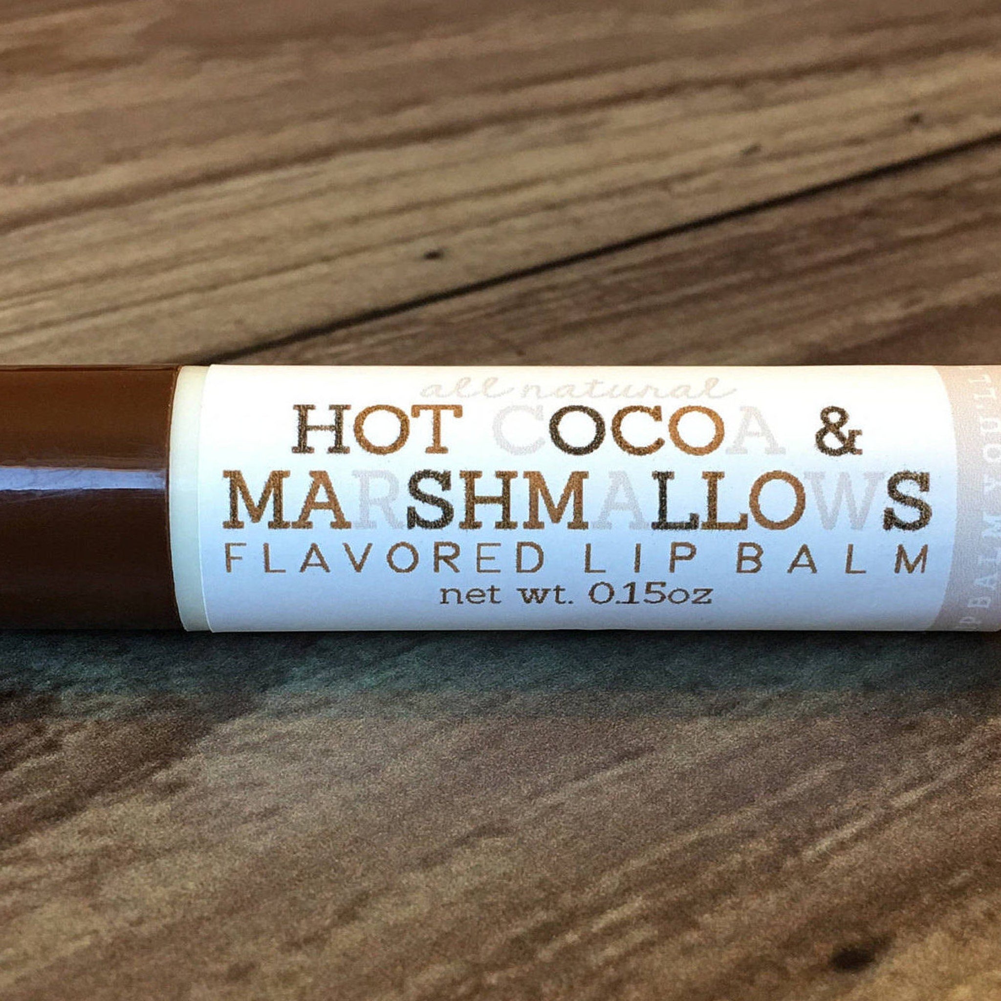 Lip balm tube with brown and white label, wooden background, "Hot Cocoa & Marshmallows" text