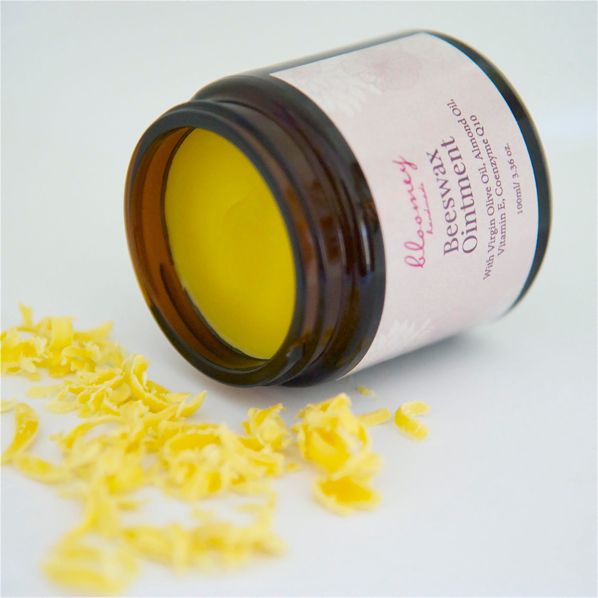 Beeswax ointment in a brown glass jar with yellow contents and yellow shavings, bloomey brand