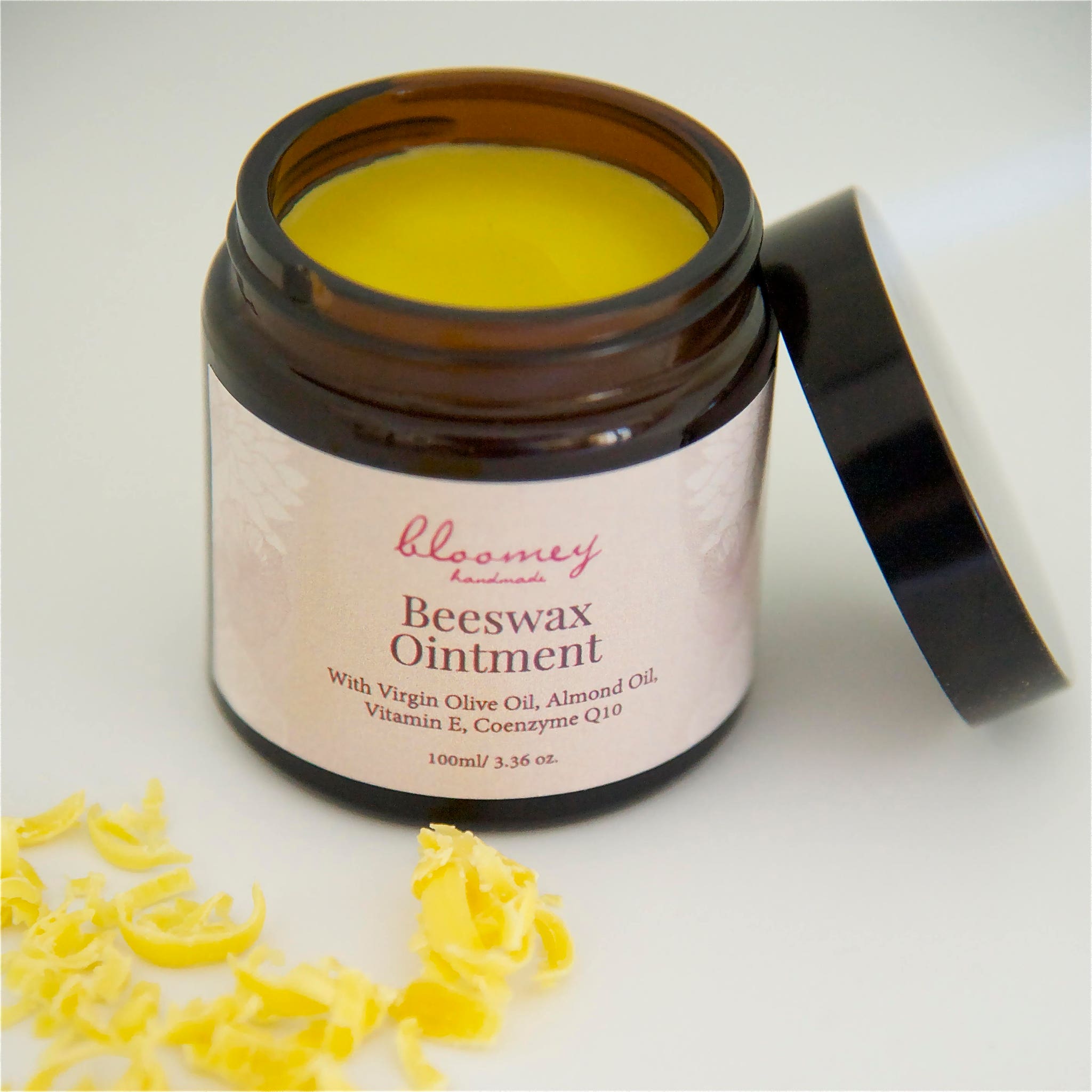 Beeswax ointment in a brown glass jar with yellow contents and black lid, "bloomey handmade" label visible