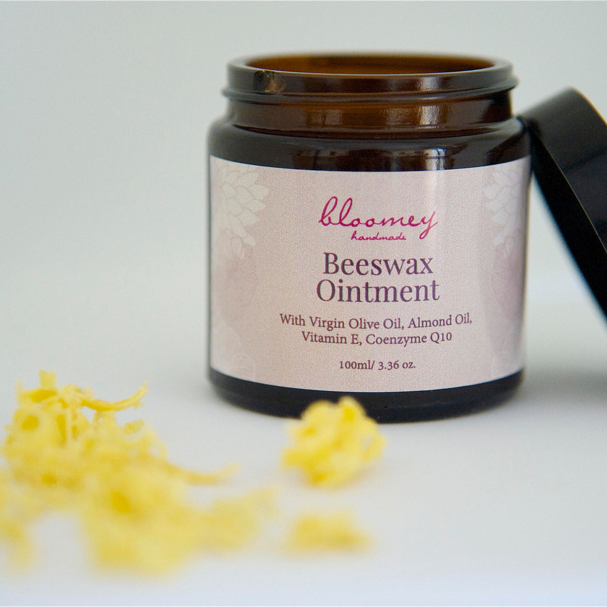Beeswax ointment in brown glass jar with black lid, "bloomey handmade" label, and yellow wax pieces