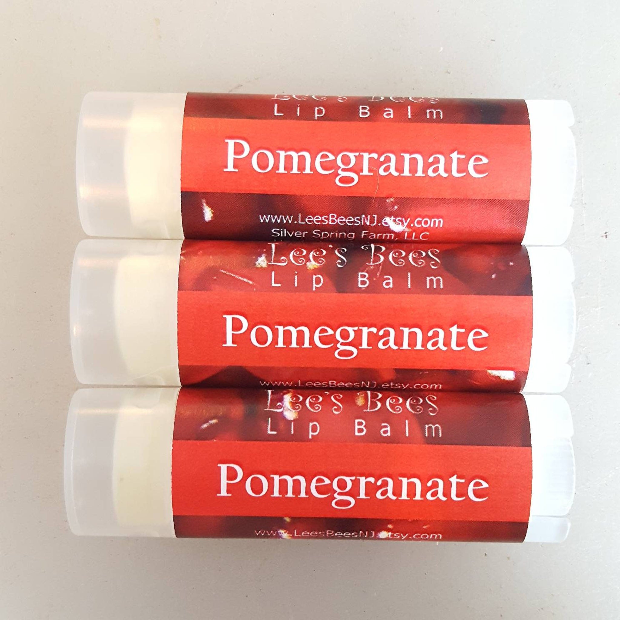 Lip balm tubes with red and white labels, Lee's Bees brand, showing Pomegranate text