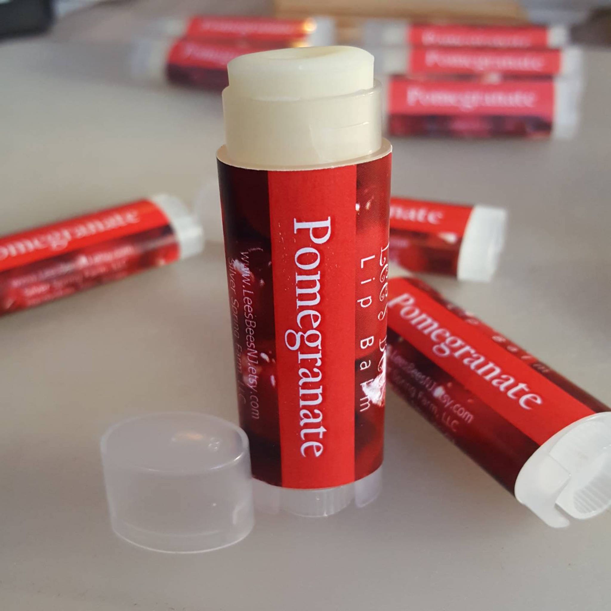 Lip balm with red label, white text, and clear cap, "Pomegranate" visible