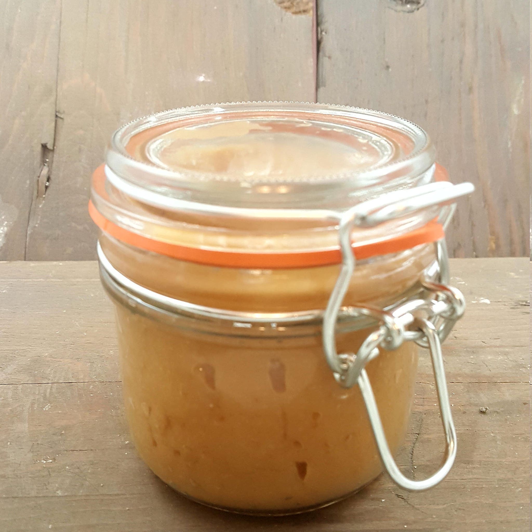 Jar of preserves with clear glass, orange seal, and metal clasp on wooden surface