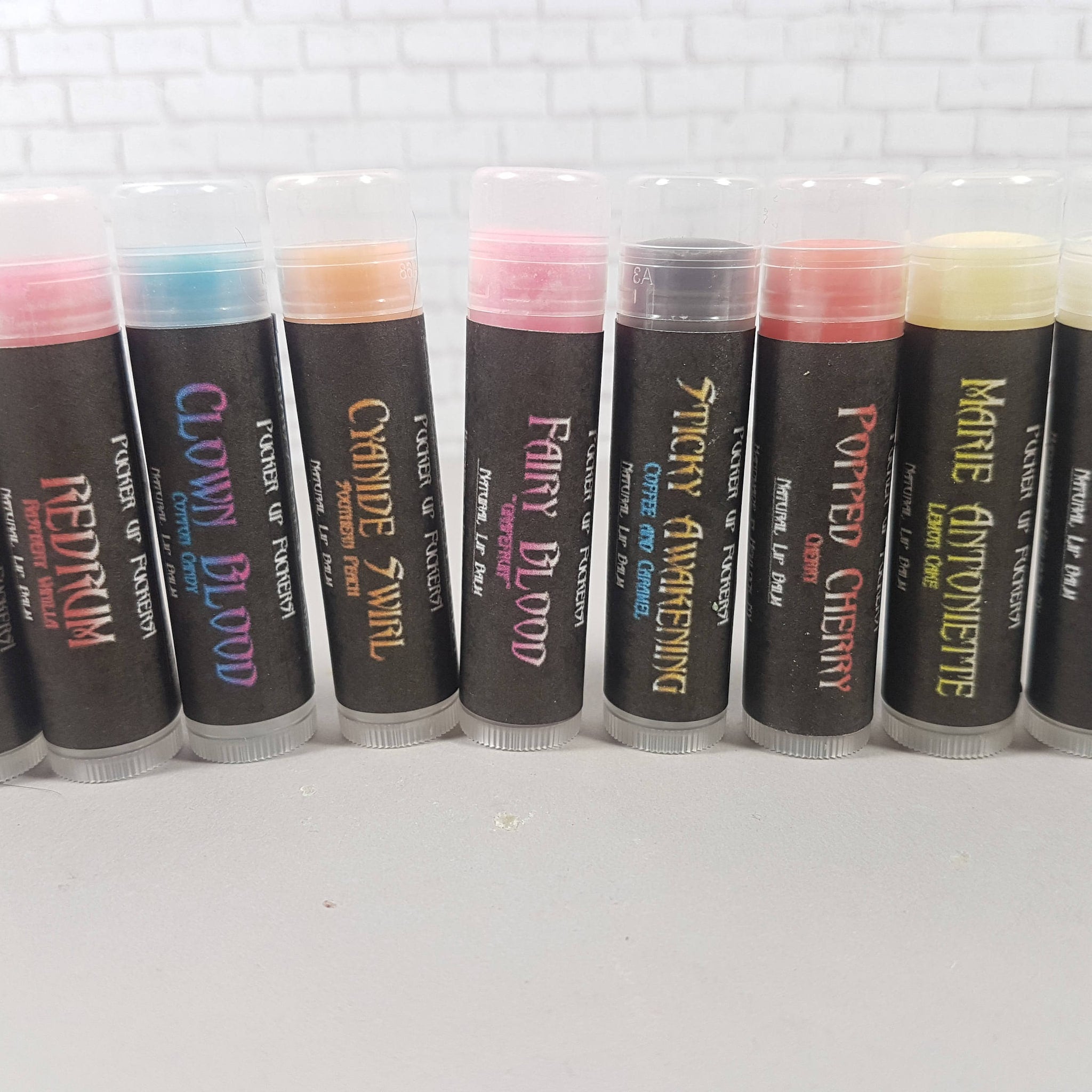 Lip balm tubes in various colors with black labels and clear caps, brand text visible