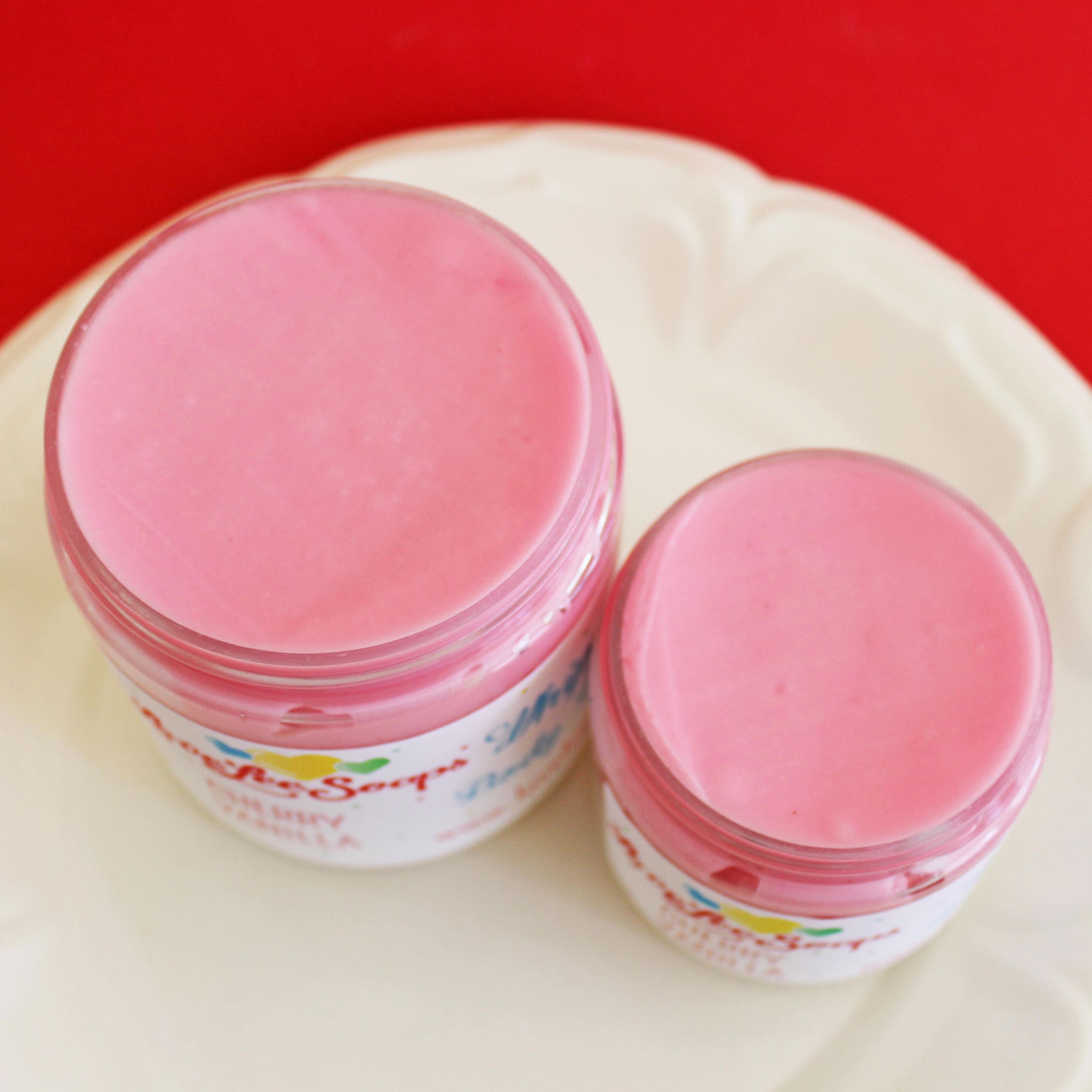 Hand scooping whipped cherry vanilla body butter from jar, showing creamy texture against skin