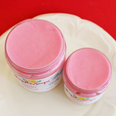Hand scooping whipped cherry vanilla body butter from jar, showing creamy texture against skin