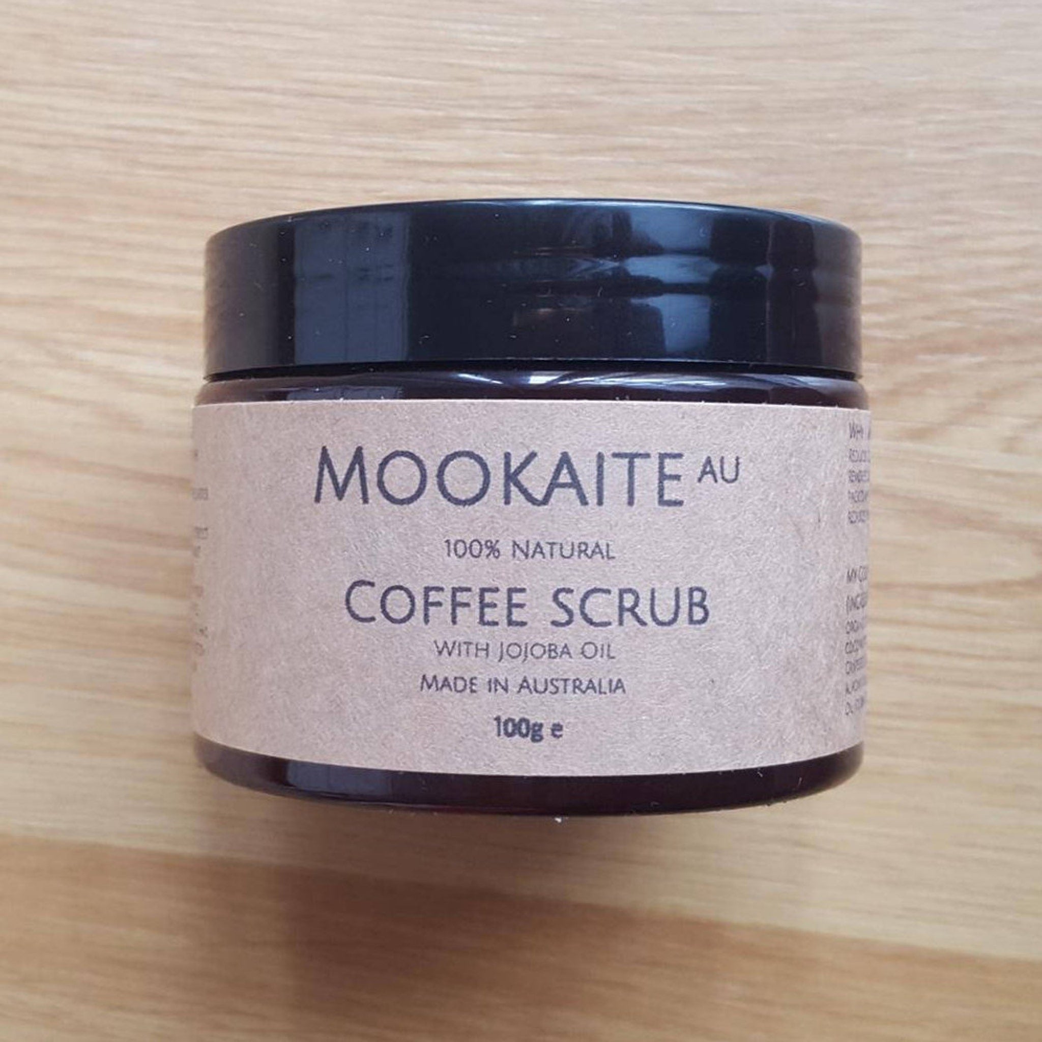 Coffee scrub jar with black lid, brown label, and MOOKAITE AU text visible on a wooden surface