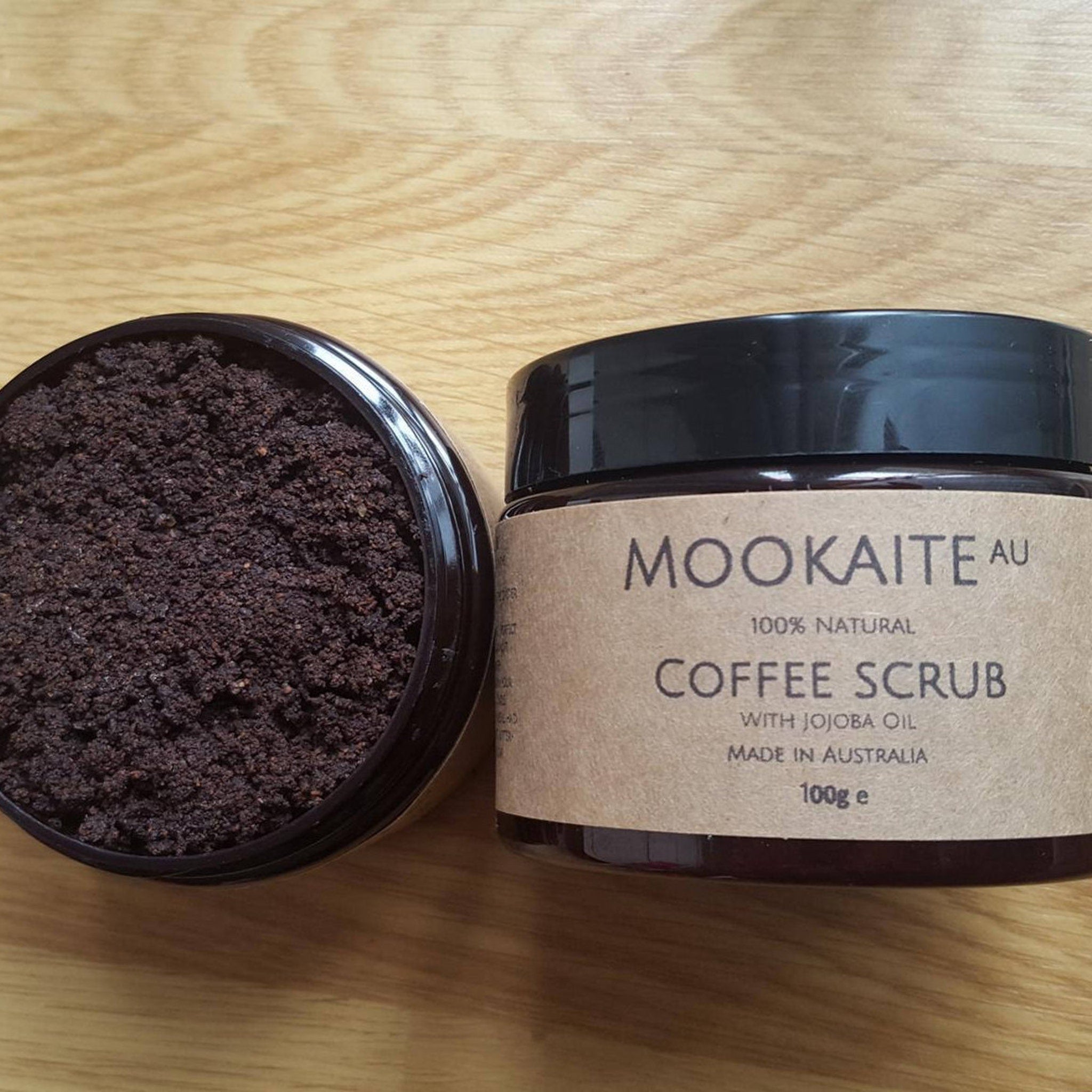 Coffee scrub with dark brown granules in black jar, "MOOKAITE AU" label visible on brown jar