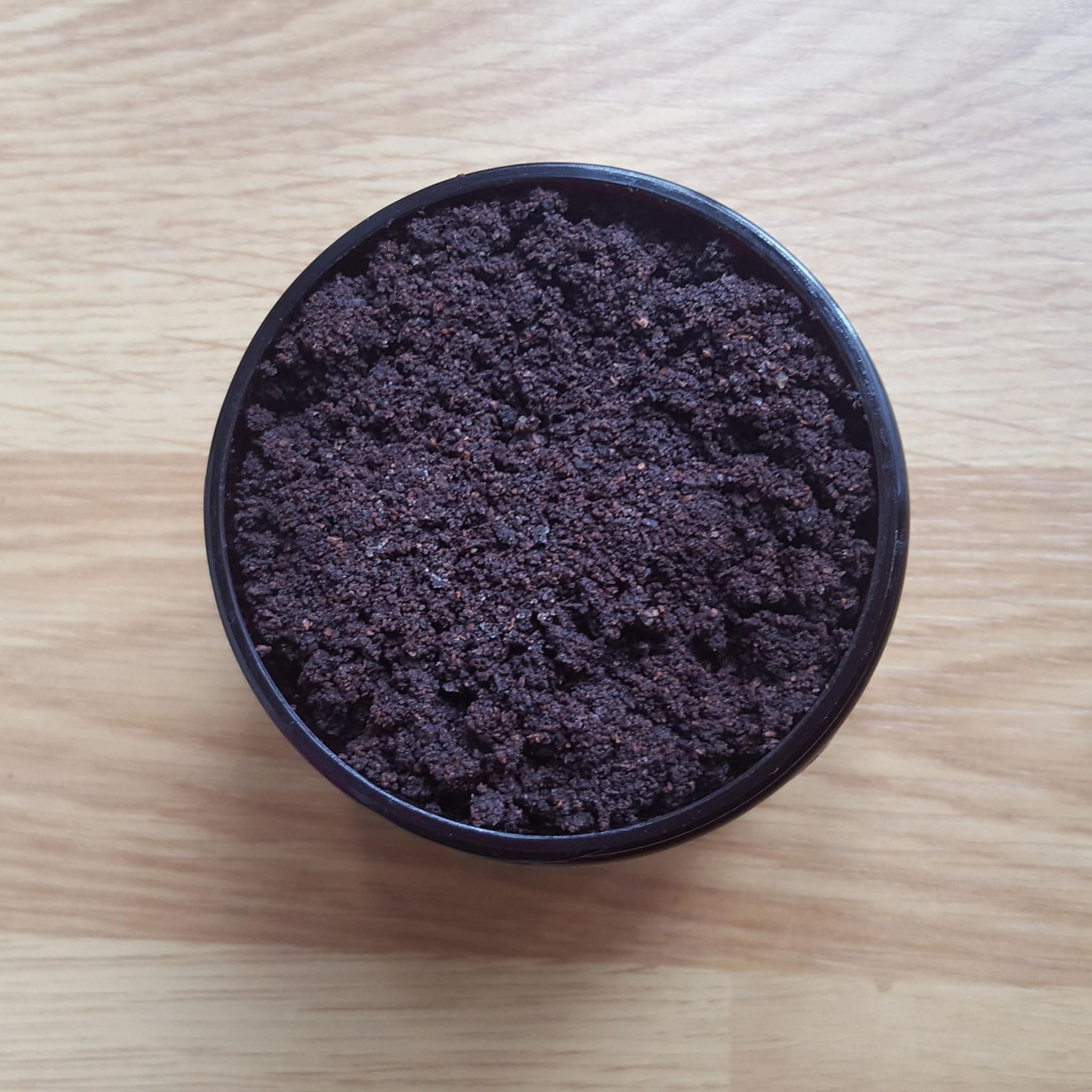 Ground dark brown substance in black container on wooden surface