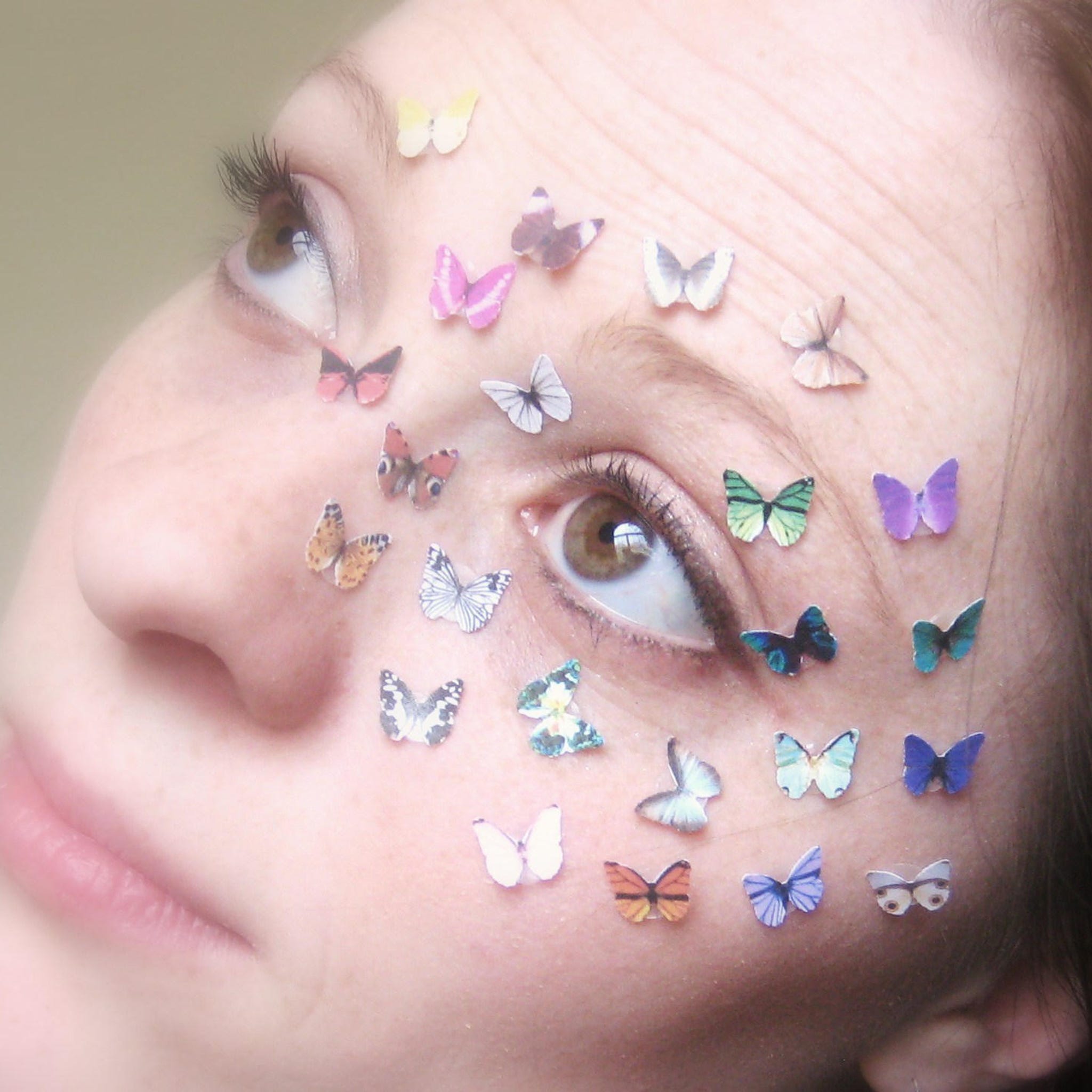 Side view of three white glitter butterfly eyeshadow stickers with delicate wing details on clear adhesive backing