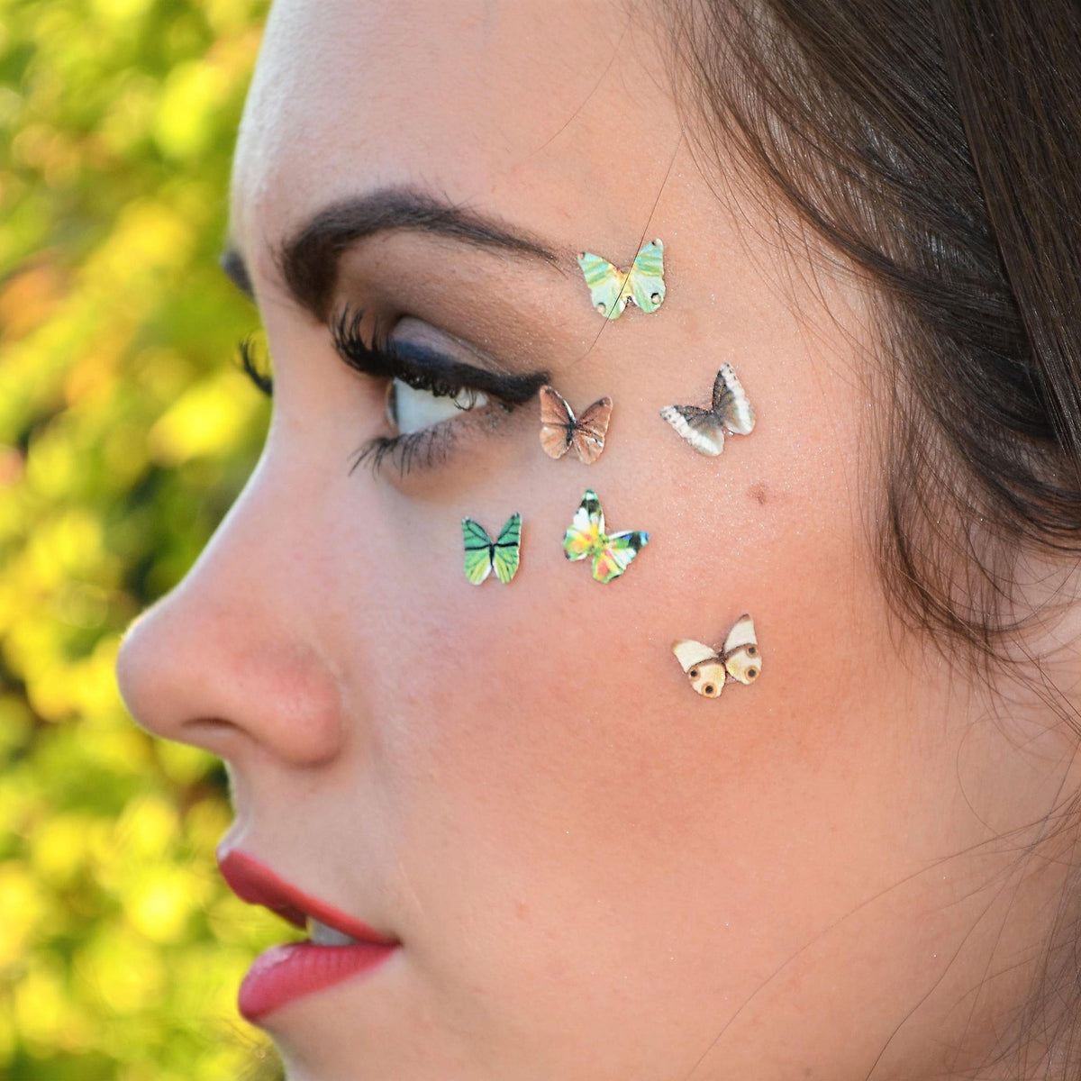 Three white glitter butterfly eyeshadow stickers with delicate wing patterns on clear adhesive backing