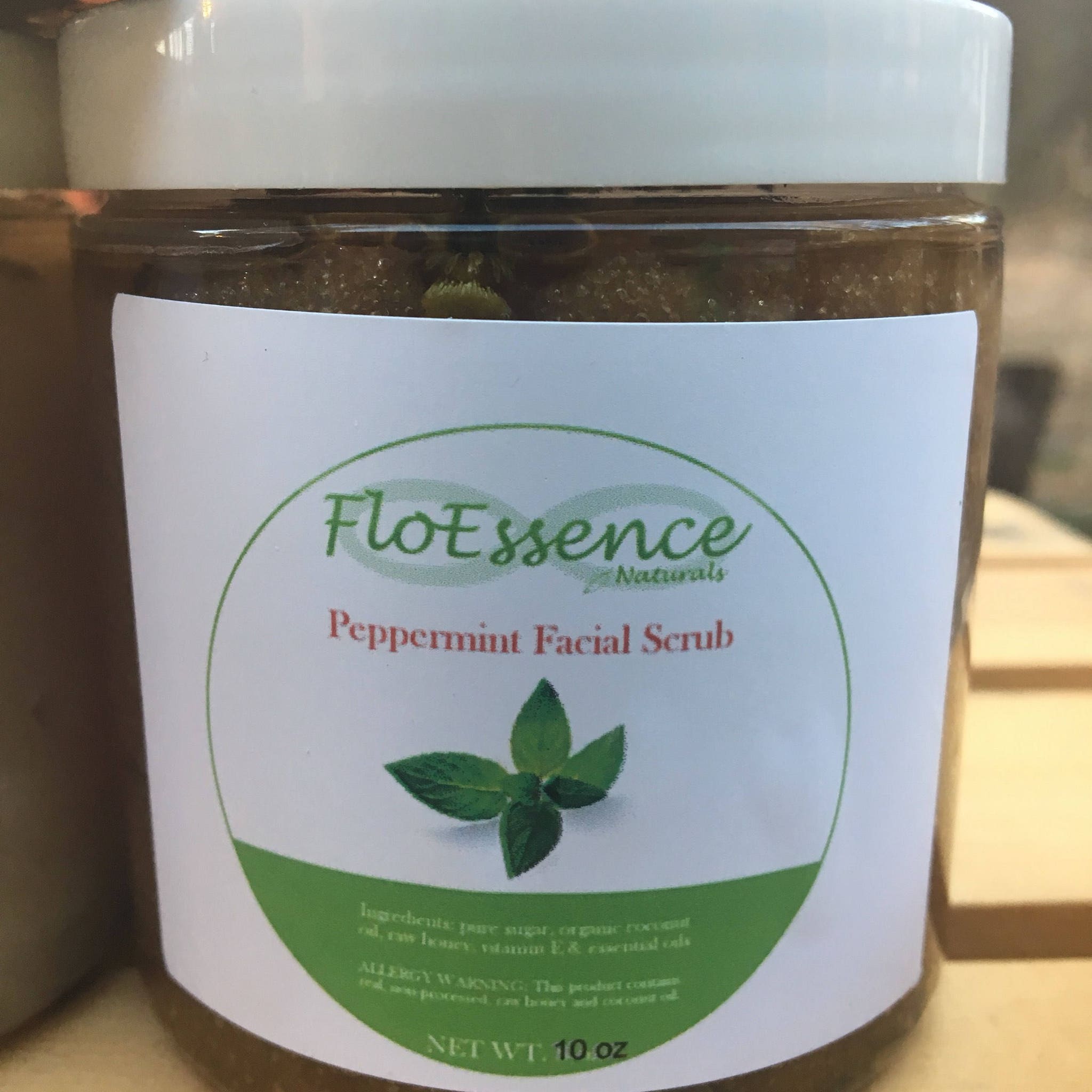 Peppermint facial scrub in clear jar with white lid, FloEssence label, and green accents