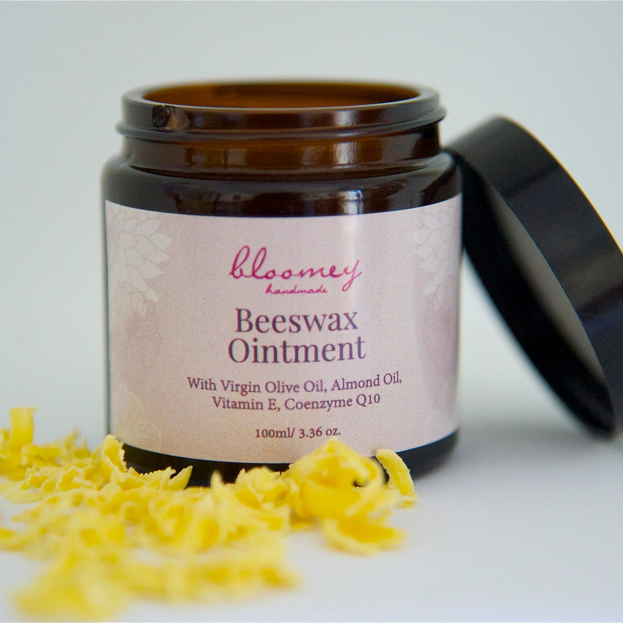 Beeswax ointment in brown glass jar with black lid, yellow wax shavings, and "bloomey" label