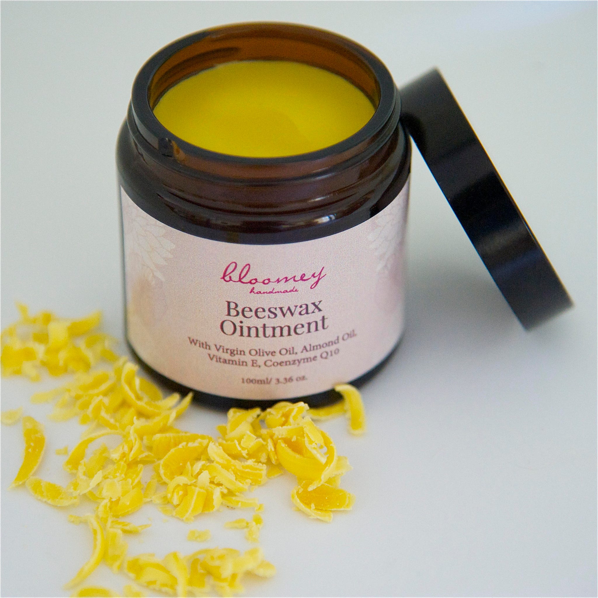 Beeswax ointment in brown jar with yellow contents, black lid, and "bloomey handmade" label on white surface