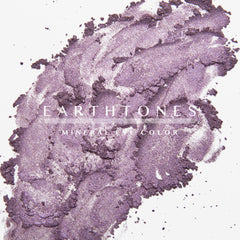 Woman applying plum mineral eyeshadow with a fluffy brush to eyelid, showcasing rich purple pigment blend