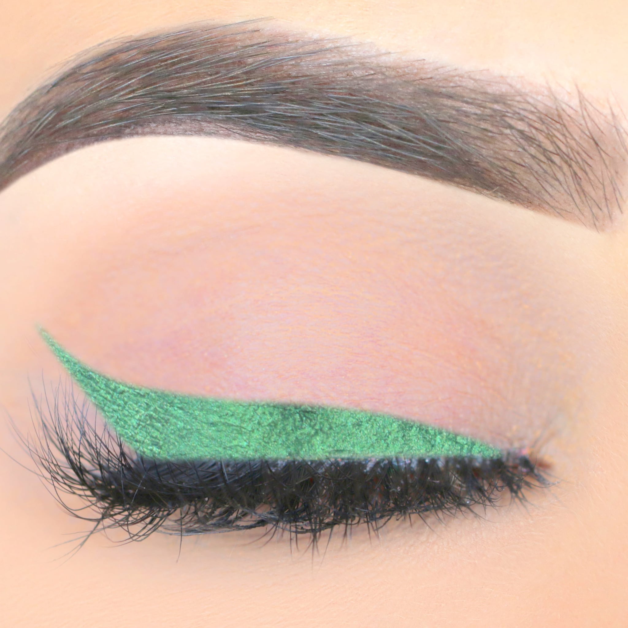 Green liquid eyeliner with winged tip on eye with black lashes and eyebrow