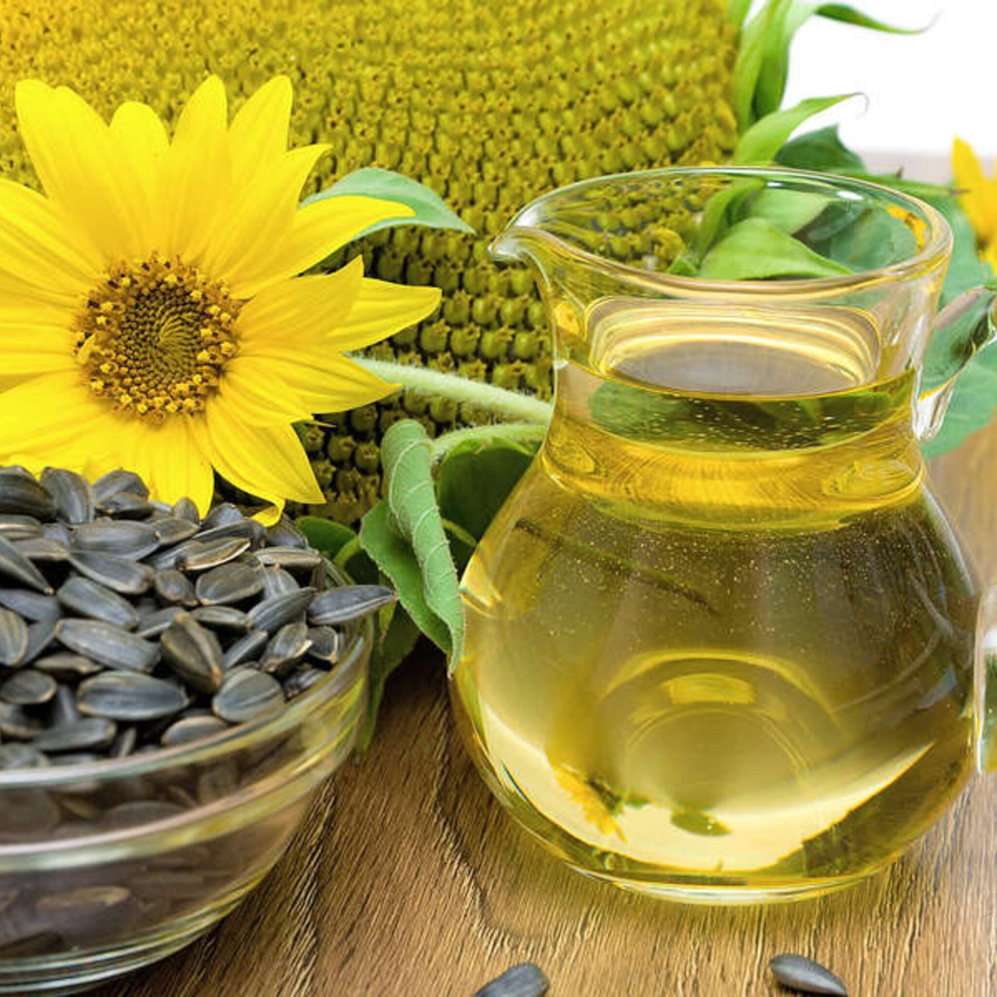 Sunflower oil in a glass pitcher with yellow liquid and seeds in a bowl on a wooden surface
