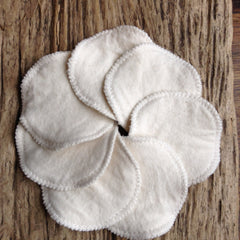 Reusable cotton rounds, white organic cotton, stitched edge, arranged in a circle on wood surface
