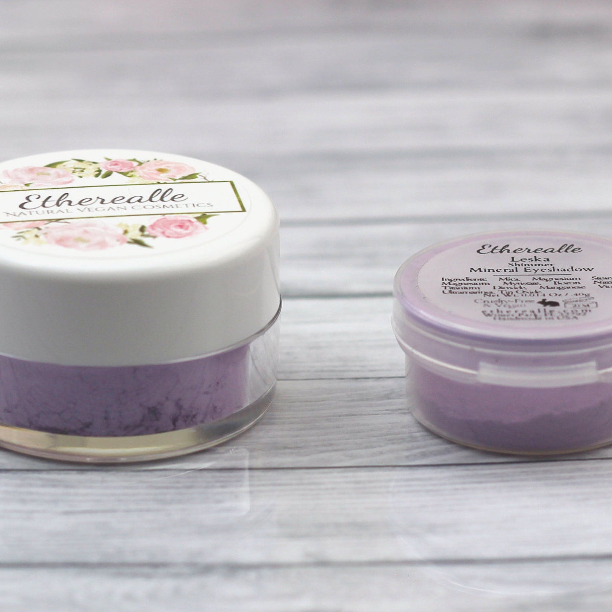 Eyeshadow pots with white and clear containers, purple powder, and Etherealle branding on top