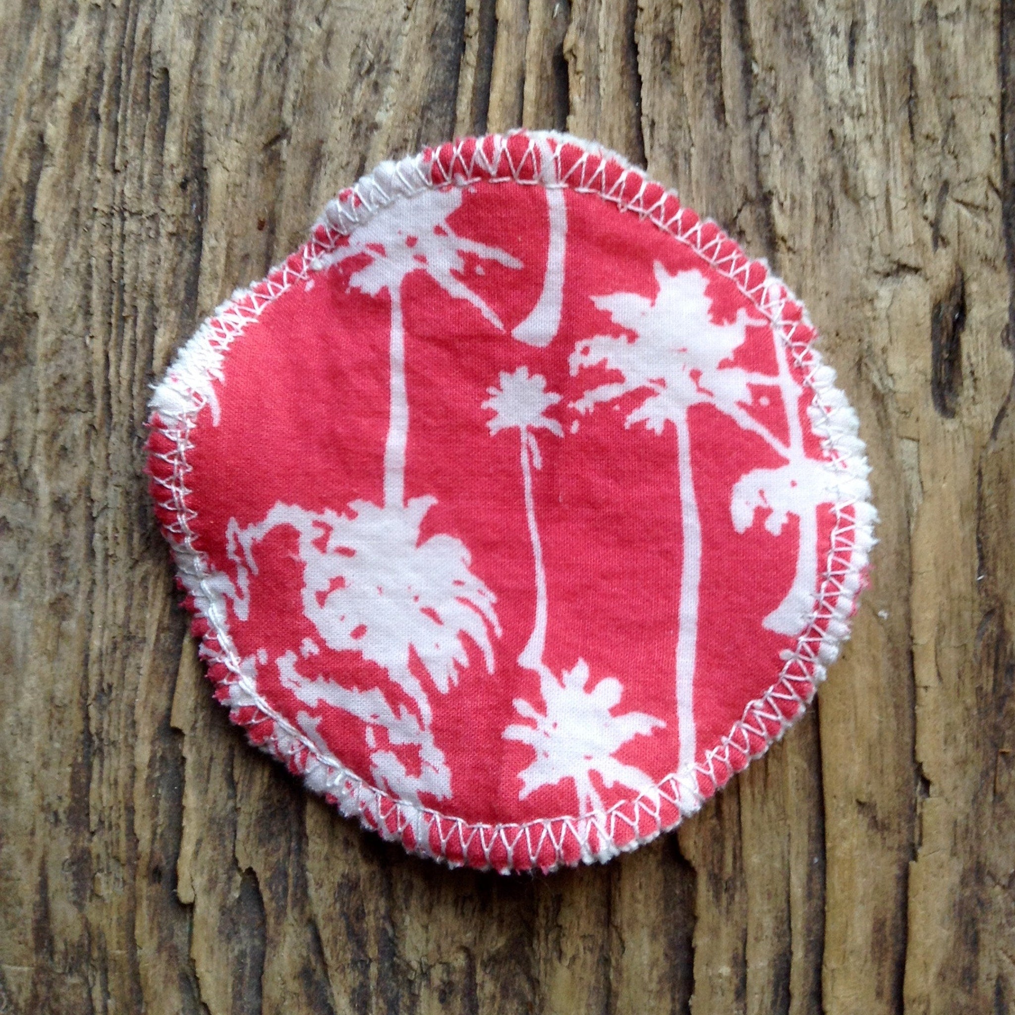 Reusable pad with red palm tree pattern, white stitching, and round shape