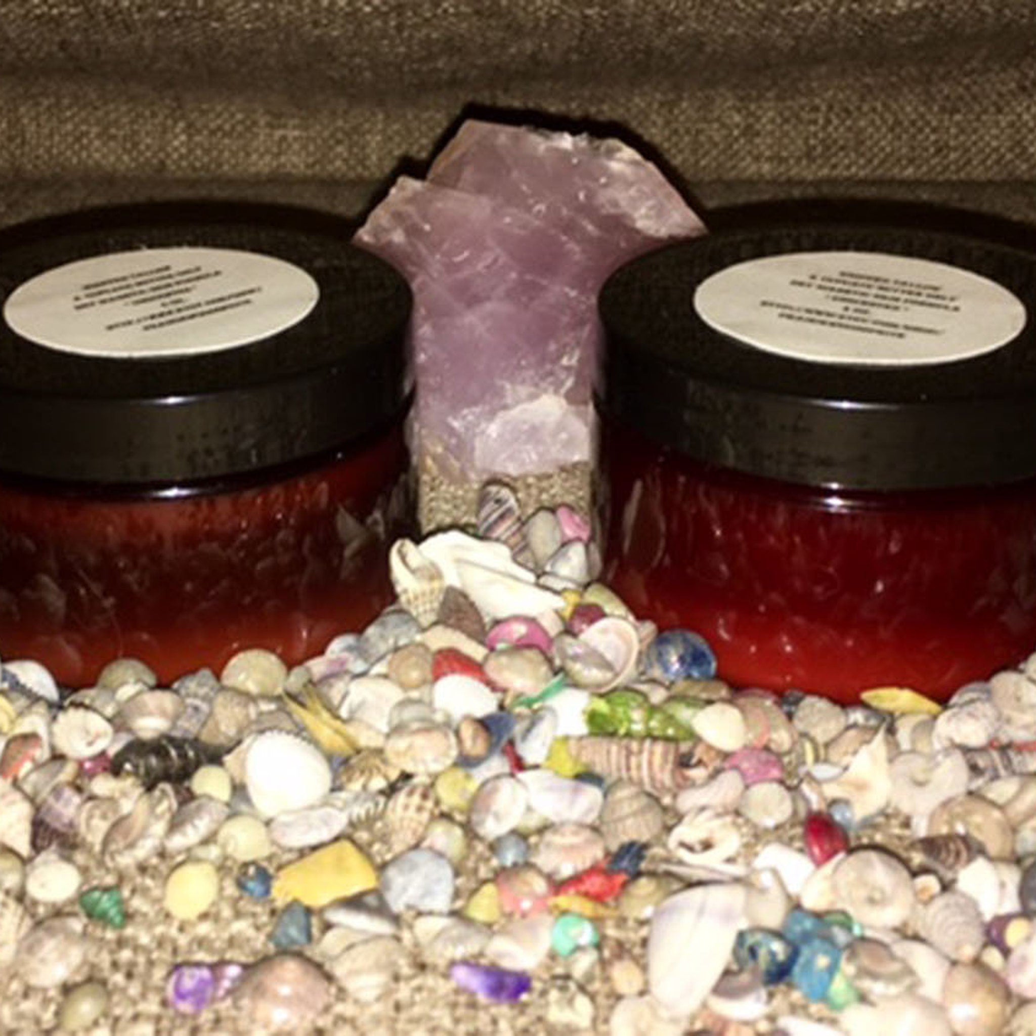 Jarred product with black lids, red contents, and white labels, surrounded by shells and crystals
