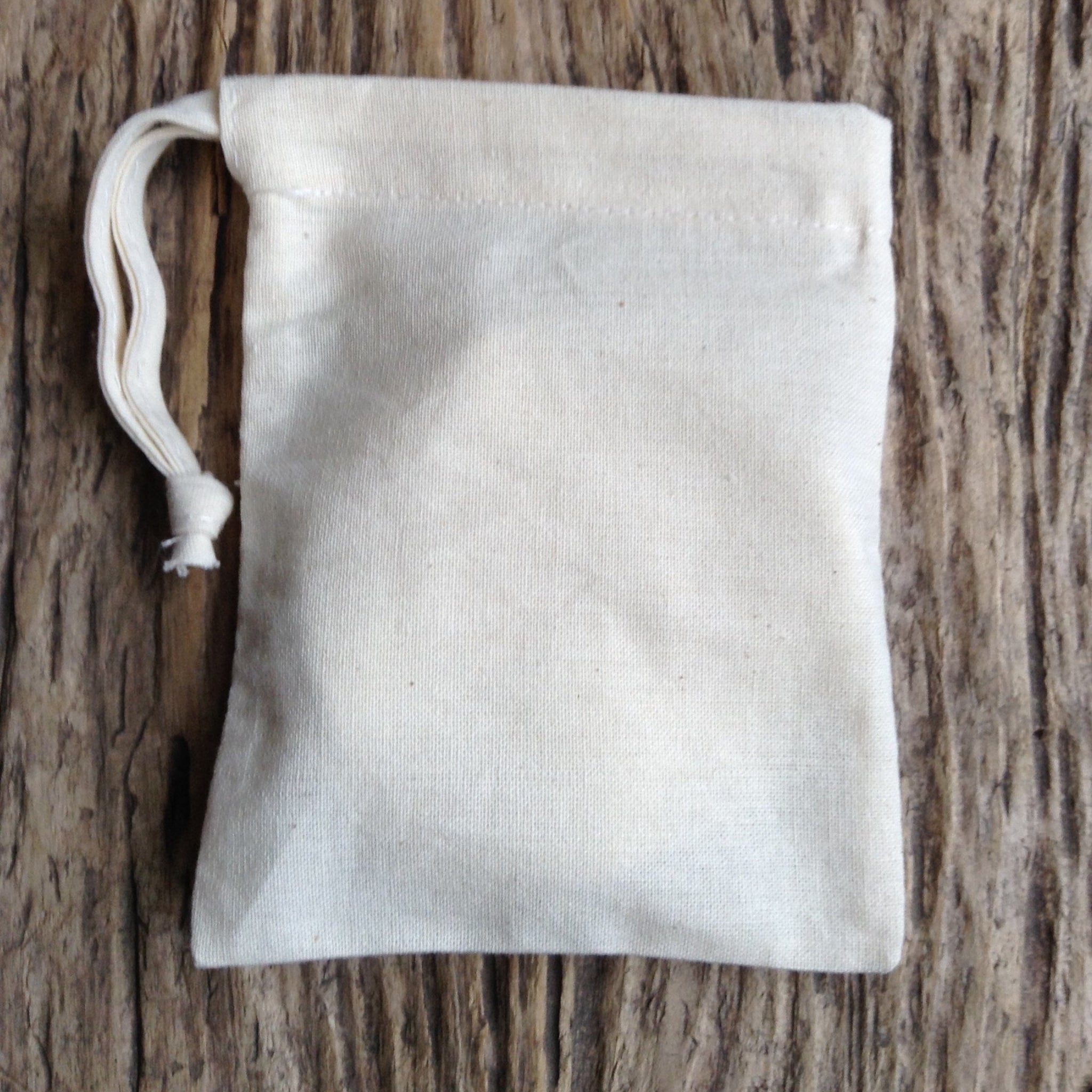Drawstring bag, off-white canvas, knotted drawstring closure, on wood surface