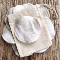 Reusable cotton pads with white cotton and beige bag, on wooden surface