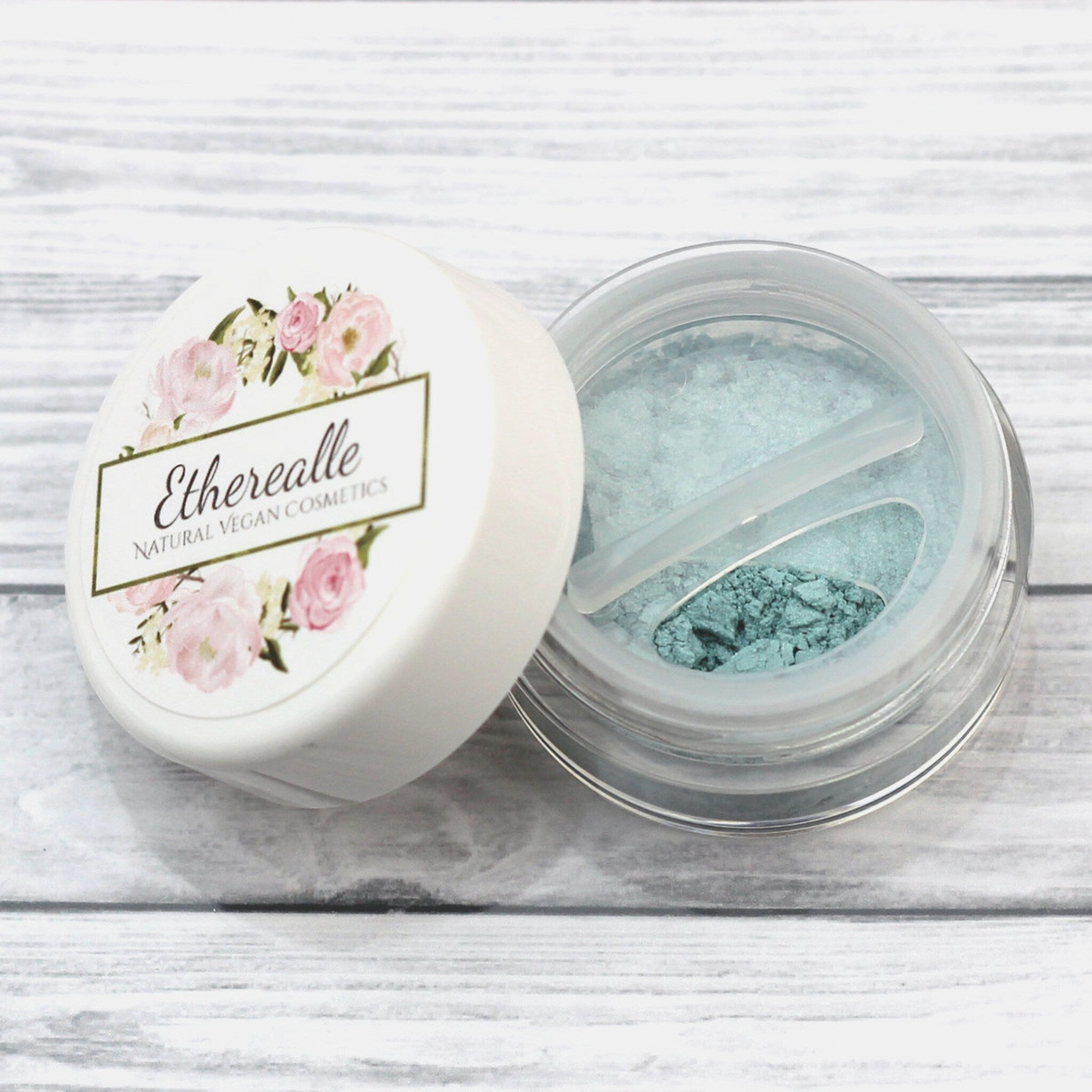 Close-up of shimmering frosty aqua blue eyeshadow being applied with a brush for a bold, metallic eyelid look.