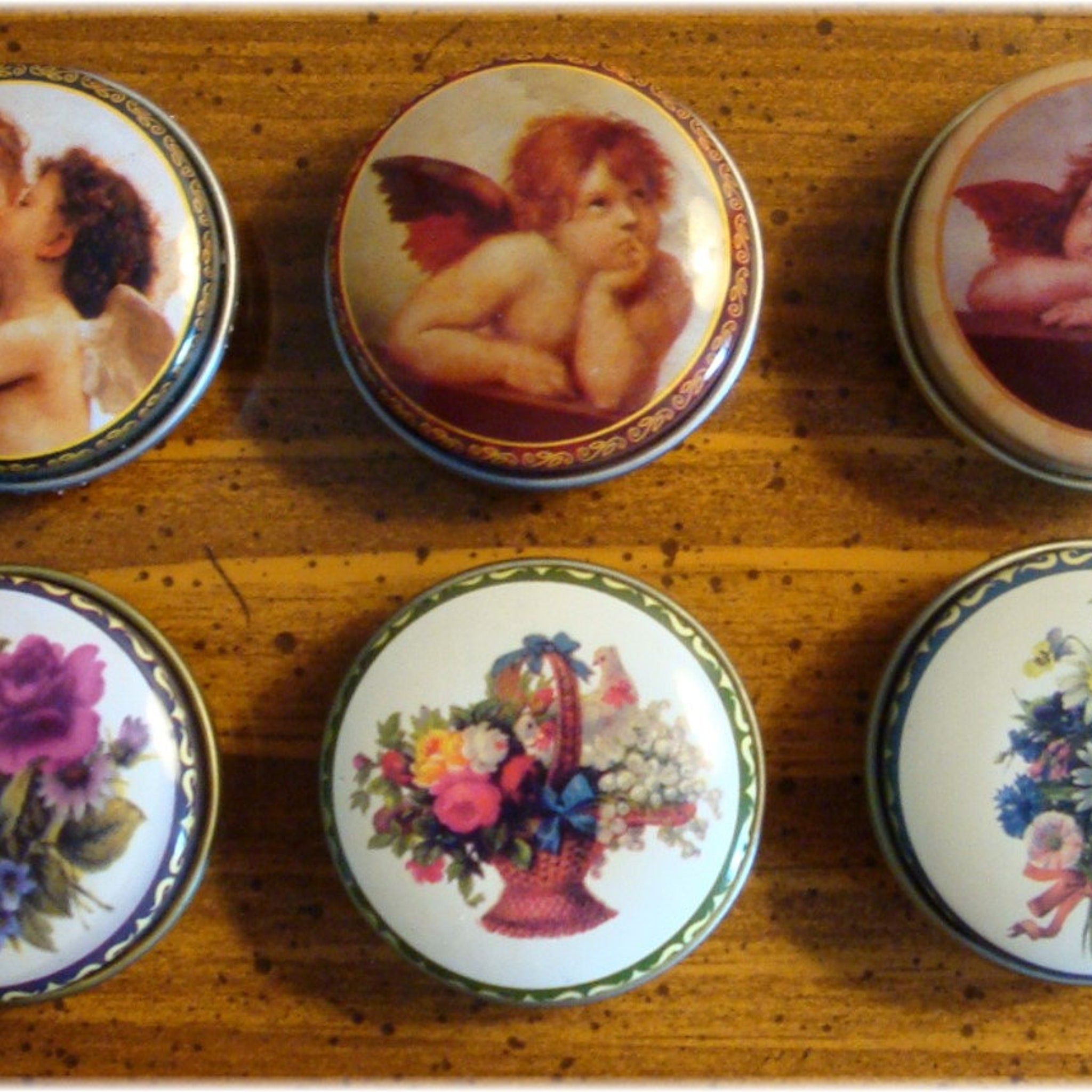 Round decorative tins with floral and cherub designs, metal rims, and painted details